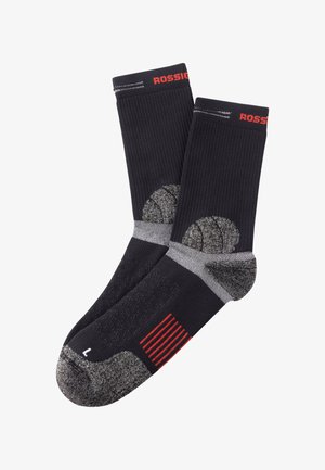 Calcetines deportivos negros con textura acanalada, acentos grises, refuerzo en el talón y la puntera, y una marca roja. Tamaño indicado como 'L' en la puntera.