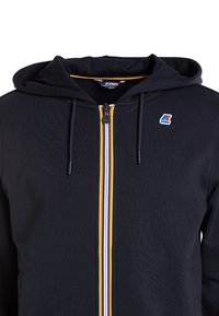 Sweat-shirt à capuche noire avec une fermeture éclair sur le devant, présentant des rayures multicolores et un petit logo sur la poitrine. Texture douce et design décontracté.