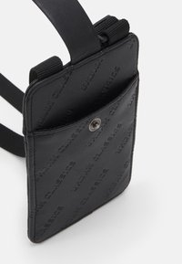Black crossbody bag made of textured synthetic material with embossed "URBAN CLASSICS" branding and a snap closure. Adjustable strap included.