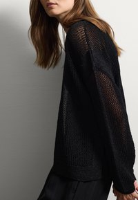 Suéter negro de punto con un tejido texturizado y abierto, y mangas largas. Presenta un dobladillo y puños acanalados, destacando un diseño ligero y aireado.