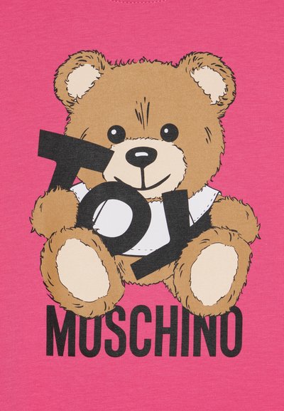 Rozā audums attēlo multfilmu lāci, kas tur melnu zīmi "TOY". Zem lāča drošā rakstā ir uzrakstīts "MOSCHINO". Lācis izskatās mīksts un teksturēts.