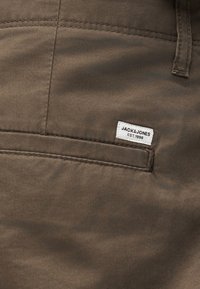 Καφέ παντελόνι από ύφασμα με τσέπη και λευκή ορθογώνια ετικέτα της μάρκας Jack & Jones ραμμένη πάνω από το άνοιγμα της τσέπης.