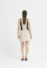 Model purtând un top fără mâneci, ajustat, de culoare crem cu un design gradient negru, asortat cu o fustă mini bej deschis și sandale cu toc negre.