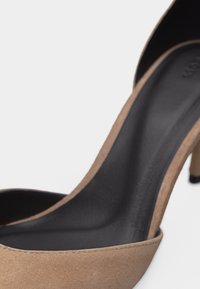 Μπεζ σουέντ ψηλοτάκουνο παπούτσι με μαύρη εσωτερική σόλα και μυτερή μύτη, εμφανιζόμενο σε κοντινή λήψη λεπτομέρειας.