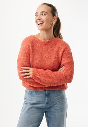 Maglione lavorato a maglia di un arancione brillante con una vestibilità morbida e una texture pesante. Maniche lunghe e orlo a costine abbinati a jeans azzurri.