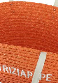Bolso de paja trenzada naranja con asas blancas. Presenta una superficie texturizada y el nombre de la marca bordado. El interior no tiene forro y es espacioso.