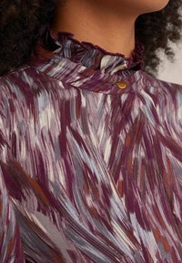 Purple patterned fabric with streaks of gray and orange. Ruffled collar detail and a small gold button accent at the neckline.
