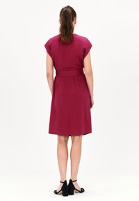 Vestido ceñido en burdeos, con mangas cortas y un corte a la altura de la rodilla. Textura de tela suave y detalles de costura discretos en la cintura.