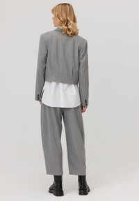 Szary krótki żakiet na białej koszuli, zestawiony z szerokimi, szarymi spodniami. Widoczne czarne botki za kostkę; materiał gładki, o fakturze.