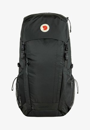 Mochila de nailon negra con un gran compartimento principal, correas ajustables, bolsillos laterales de malla y un logo circular en el panel frontal.
