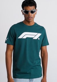 Teal bomulds t-shirt med et stort hvidt Formel 1-logo på forsiden, rund halsudskæring og korte ærmer. Slim fit, glat tekstur.