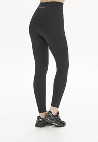 Svarta högmidjade leggings med en slät textur och en åtsittande design, som matchas med svarta träningsskor i blandade material med subtila detaljer.