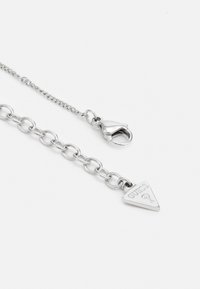 Collana in argento con maglie circolari, chiusura a moschettone e pendente triangolare inciso con la scritta "GUESS" e un punto interrogativo.