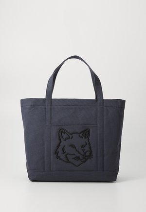 Sac en toile bleu marine avec un motif en relief d'une tête de renard sur le devant, doté de deux poignées robustes et d'une forme rectangulaire structurée.