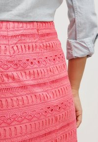 Gonna ricamata rosa con ritagli a strati, caratterizzata da un design testurizzato e una cintura visibile. Il tessuto appare leggero e arioso.