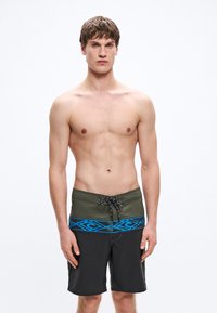 Μαύρα μαγιό σορτς με πράσινη ελαστική μέση που διαθέτει μπλε γεωμετρικό μοτίβο και ρυθμιζόμενο κορδόνι. Λεία υφή.