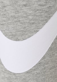 Tessuto grigio con un motivo a maglia testurizzato presenta un grande logo Nike bianco. Il design è semplice e contemporaneo, enfatizzando la curva del logo.