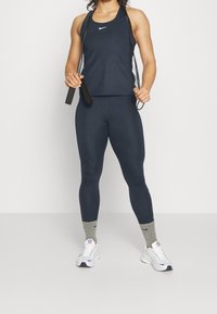 Canotta atletica blu navy e leggings aderenti, realizzati in tessuto elasticizzato. Il modello tiene una corda per saltare, indossando calze grigie chiare e sneakers bianche.