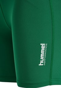 Grønne atletikshorts med synlige syninger og hvid "hummel PERFORMANCE" branding på siden.