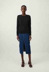 Top negro de manga larga, falda midi de mezclilla con abertura frontal y zapatos de tacón negros con tiras. Textura suave, silueta ajustada, diseño minimalista.