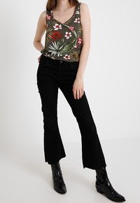 Tank top w kwiatowym nadrukiem w ciemnooliwkowym kolorze z jasnymi i żywymi detalami; zestawiony z czarnymi spodniami z kieszeniami i błyszczącymi czarnymi botkami.