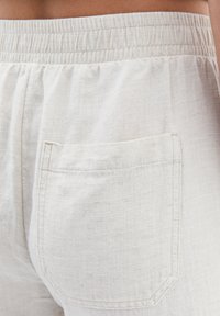 Pantalones de lino crema con cintura elástica, que presentan un solo bolsillo trasero y un diseño de tela texturizada y tejida.