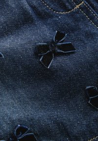 Denimstof i mørkeblå med en subtil struktur, prydet med små applikationer af sort velour i form af sløjfer og kontrasterende gule syninger.