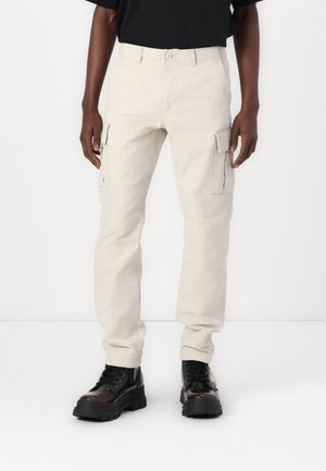 Beige cargo pants with side pockets, made of durable fabric. Fitted straight leg design. Paired with black, chunky lace-up boots.