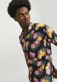 Camisa de manga corta con cuello en tela negra que presenta coloridos patrones florales en rosa, amarillo y verde, con una textura suave.