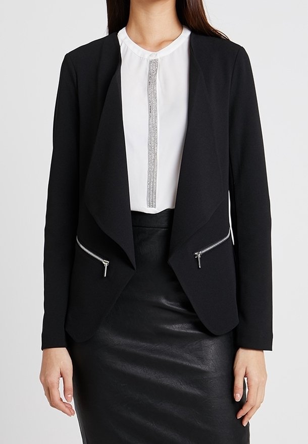 Svart blazer med draperad front, två dragkedjefickor och skräddarsydd passform. Bärs över en vit blus med en silveraccent. Texturerad svart kjol.