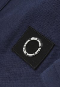 Tissu texturé bleu marine avec un patch carré noir portant un logo circulaire blanc avec l'inscription "RELLIX THE ORIGINAL."