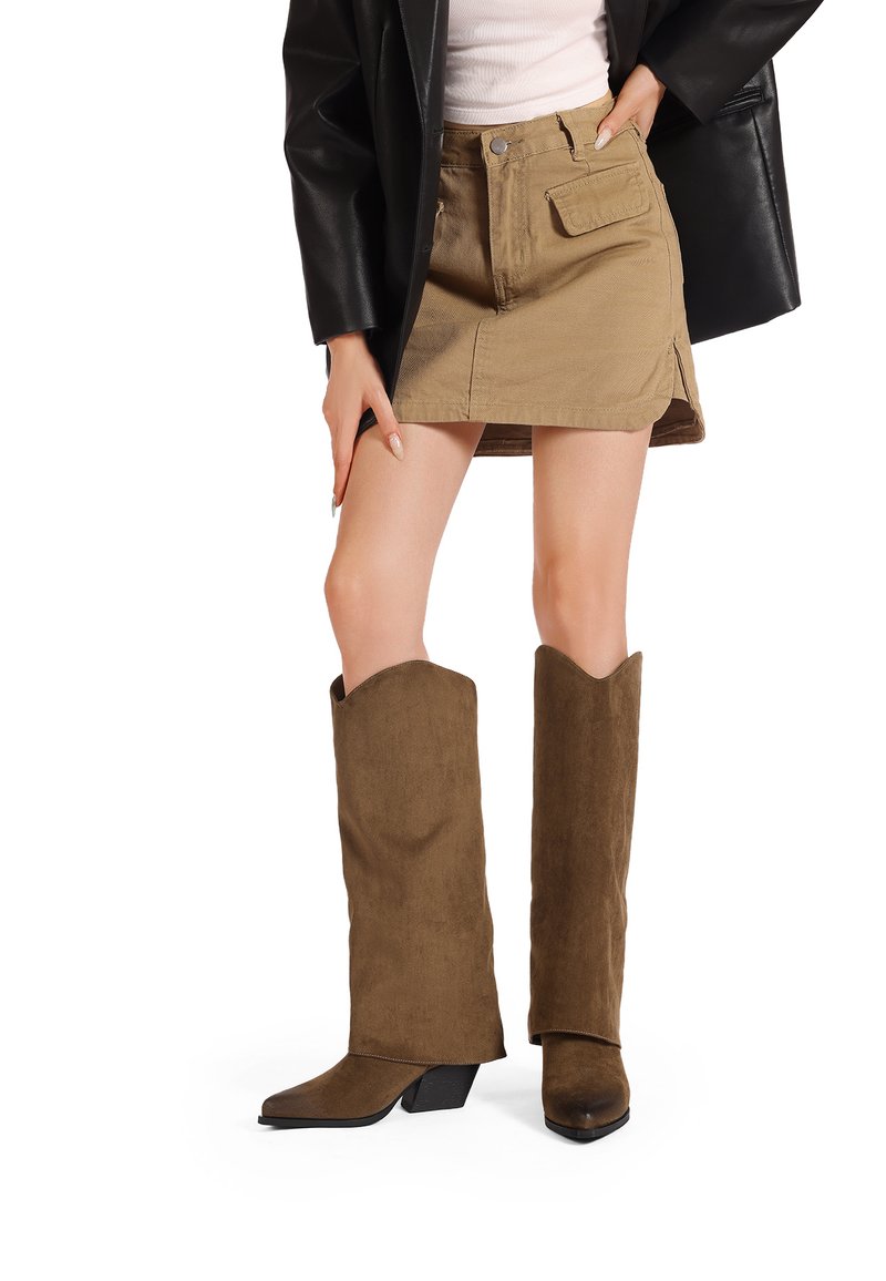 Stivali alti al ginocchio in suede marrone con punta affilata e tacco leggero, abbinati a una mini gonna khaki con design di tasche frontali.