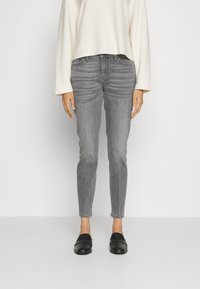 Jeans de denim grises con un corte ajustado, cintura alta, ligero desgaste y un dobladillo limpio, combinados con zapatos negros tipo slip-on y una blusa oversized color crema.