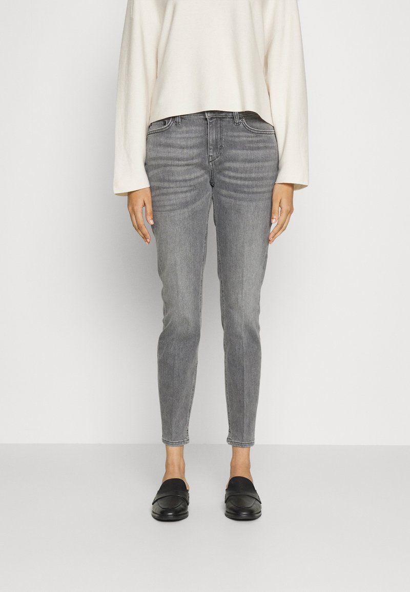 Jeans de denim grises con un corte ajustado, cintura alta, ligero desgaste y un dobladillo limpio, combinados con zapatos negros tipo slip-on y una blusa oversized color crema.