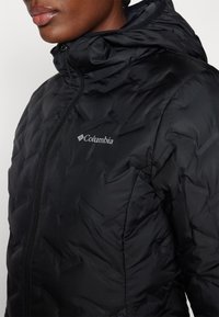 Svart pufferjakke med quiltet tekstur, glidelås og hette. Har et sølvfarget Columbia-logo på brystområdet.
