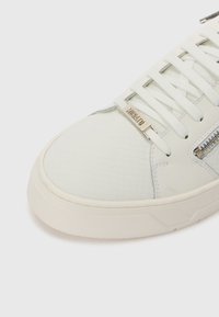Tenis alb cu un upper texturat și un model geometric, șireturi plate, detalii cu fermoar și o talpă din cauciuc crem.