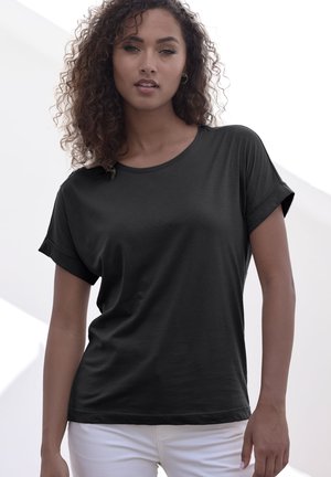 Schwarzes kurzärmliges T-Shirt mit Rundhalsausschnitt und umgeschlagenen Ärmelabschlüssen, aus glattem Material gefertigt. Das Modell trägt weiße Hosen.