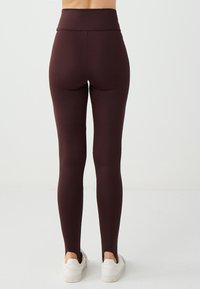 Leggings marroni realizzati in materiale elastico, dotati di un alto punto vita e di una vestibilità aderente, abbinati a sneakers bianche.