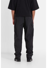 Svart oversized t-shirt i kombination med svarta cargobyxor. Byxorna har en sidoficka, dragsko i slutet och en lös, texturerad kvalitet. Svarta sneakers.