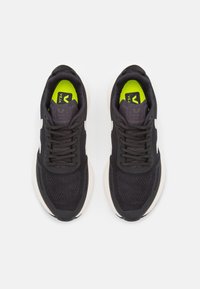 Black athletic sneakers with mesh upper, contrasting white accents, and bright green insoles. Features round laces and padded collar.
