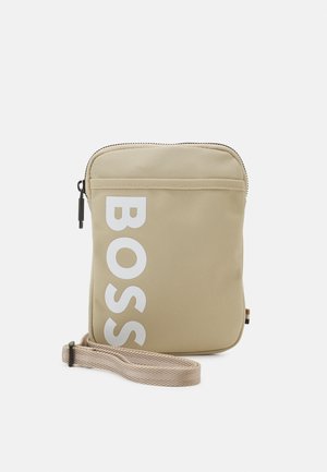 Borsa a tracolla rettangolare beige con scritta "BOSS" bianca, chiusura con cerniera superiore e tracolla regolabile abbinata su sfondo bianco.