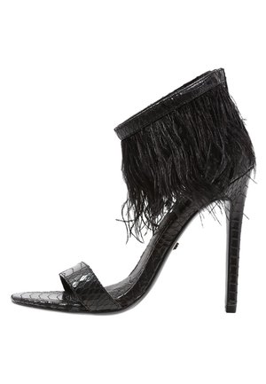 Sandalia negra de tacón alto con textura de piel de serpiente, tirante en el tobillo adornado con flecos de plumas negras y diseño de punta abierta.
