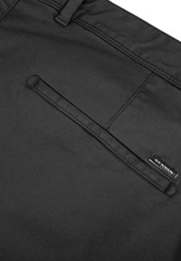 Zwarte stoffen broek met een soepele textuur, voorzien van een achterzak en een klein merklabel nabij de tailleband. Eenvoudig en functioneel ontwerp.