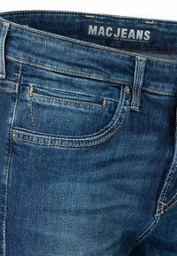 Jeans aus Denim in einem dunklen Blauton mit einer verwaschenen Optik. Zu den Merkmalen gehören ein Fünf-Taschen-Design, goldene Nähte und ein Markenlabel am Bund.