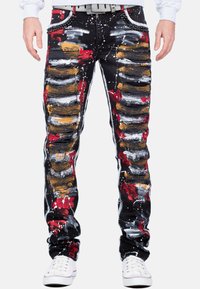 Jeans noirs usés avec de multiples éclaboussures de peinture en rouge, blanc et or. Coutures décoratives apparentes et une coupe fuselée, avec une taille décorative.