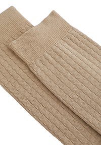 Mangas para piernas de punto en color beige con una textura acanalada y un patrón cuadrado, que cuentan con un borde superior doblado para mayor comodidad.