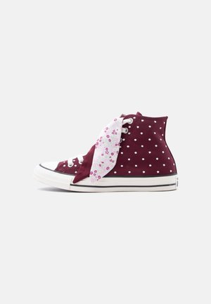 Maroon high-top sneaker with white polka dots, white rubber sole, and a pink floral-patterned cloth tied around the laces.
