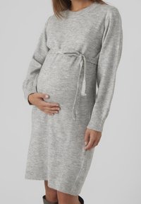 Ljust grått stickat gravidklänning, knälångt, med långa ärmar, rund halsringning och en framknutbar midja för justerbar passform.