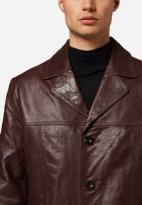 Braune Lederjacke mit Kragen, ausgestattet mit einem Knopfverschluss, glatter Textur und sichtbaren Nähten.