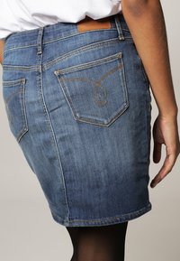 Jeanskjol i medelblått med synliga sömmar. Har en kort fåll, femfickorsdesign och dekorativ brodering på bakfickan.